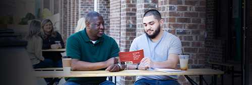 Two men reading the Steps To Peace With God booklet outside of a coffee shop