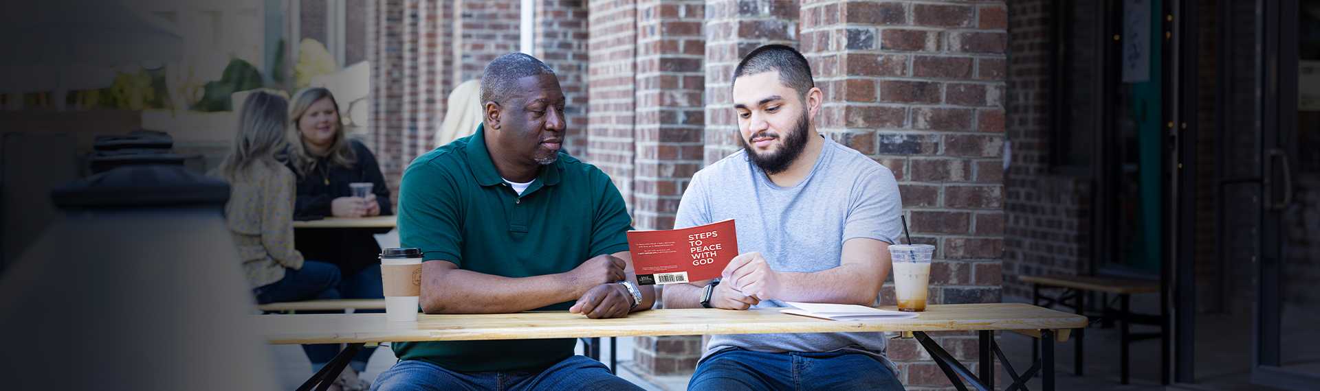 Two men reading the Steps To Peace With God booklet outside of a coffee shop